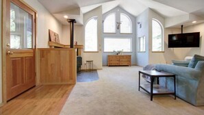 Un salón amplio con un aparador de madera, un televisor montado en la pared y un ventanal grande decorado con una cabeza de venado.