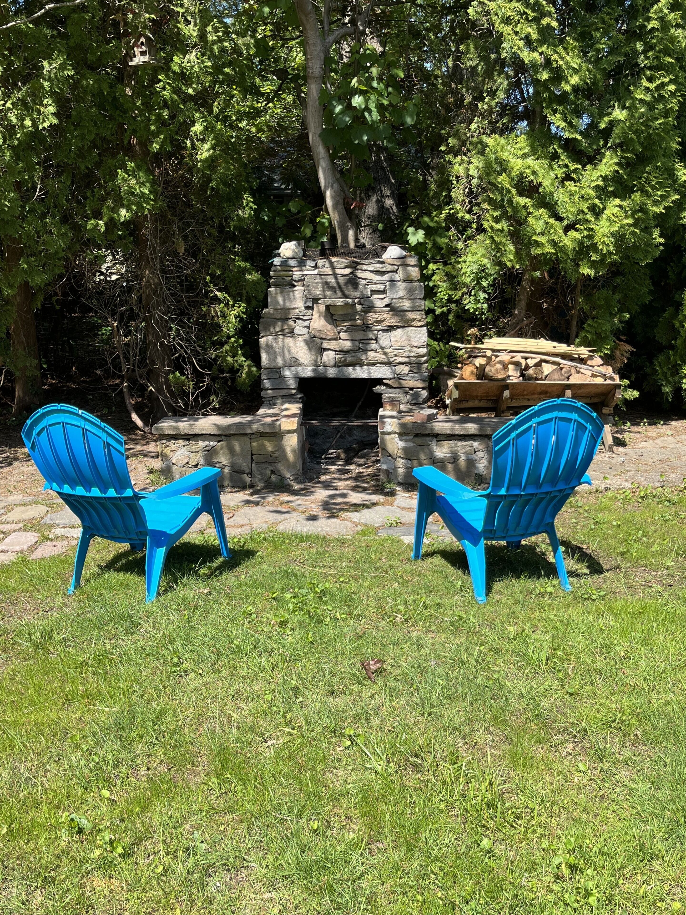 Une cheminée en pierre, devant laquelle se trouvent deux fauteuils Adirondack bleus.