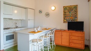 Cocina compacta con armarios blancos, estufa y comedor con sillas blancas.
