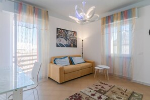 Una sala de estar con un sofá, una mesa de vidrio, una lámpara y un cuadro en la pared.