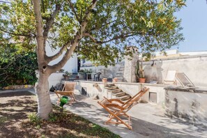 Un patio con mobiliario exterior, un árbol y una pared con escalones que llevan a una azotea.