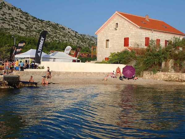 A stone building with a red roof, a swimming area with people, and flags.