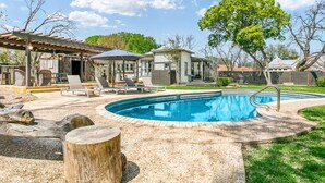 Un cortile con piscina, lettini da sole e una zona patio coperta.