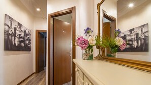 A hallway with a wooden door, a mirror, and two black-and-white cityscape paintings on the walls. - Appartamento a 200 metri dall\'Arena con 3 camere da letto e terrazzo (Verona)