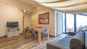 A modern living room with a wooden dining table, grey chairs, a sofa, a television, and a painting on the wall. - Appartamento a 200 metri dall\'Arena con 3 camere da letto e terrazzo (Verona)