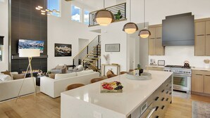 Cocina moderna con una isla central, electrodomésticos de acero inoxidable y un comedor con sofá y mesa de centro.