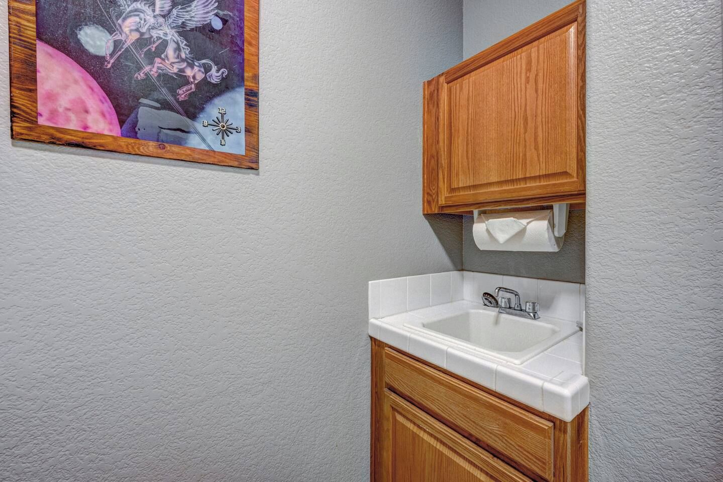 Un baño con lavamanos blanco, armarios de madera y dispensador de toallas en la pared.