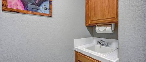 Un baño con lavamanos blanco, armarios de madera y dispensador de toallas en la pared.