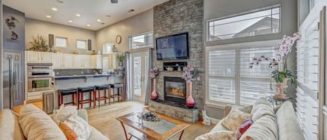 A spacious living area with a fireplace, a sofa set, a coffee table, and a television mounted above the fireplace.