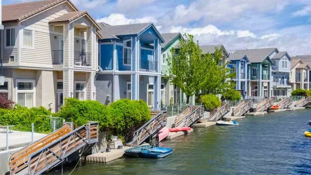Un quartier résidentiel situé au bord de l’eau, avec des immeubles à plusieurs étages, un quai où sont amarrés des bateaux et un ciel dégagé.