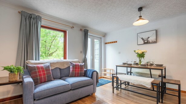 Un salon moderne avec un canapé gris, un plancher en bois, une table à manger avec des chaises et une fenêtre avec des rideaux.