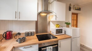 Une cuisine moderne avec des meubles blancs, une hotte en acier inoxydable, une plaque de cuisson à induction noire, un four à micro-ondes, un réfrigérateur et un plan de travail en bois.