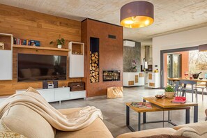 Ein modernes Wohnzimmer mit großem Flachbildfernseher, Holzvertäfelung, Kamin und Essbereich mit Tisch und Stühlen.