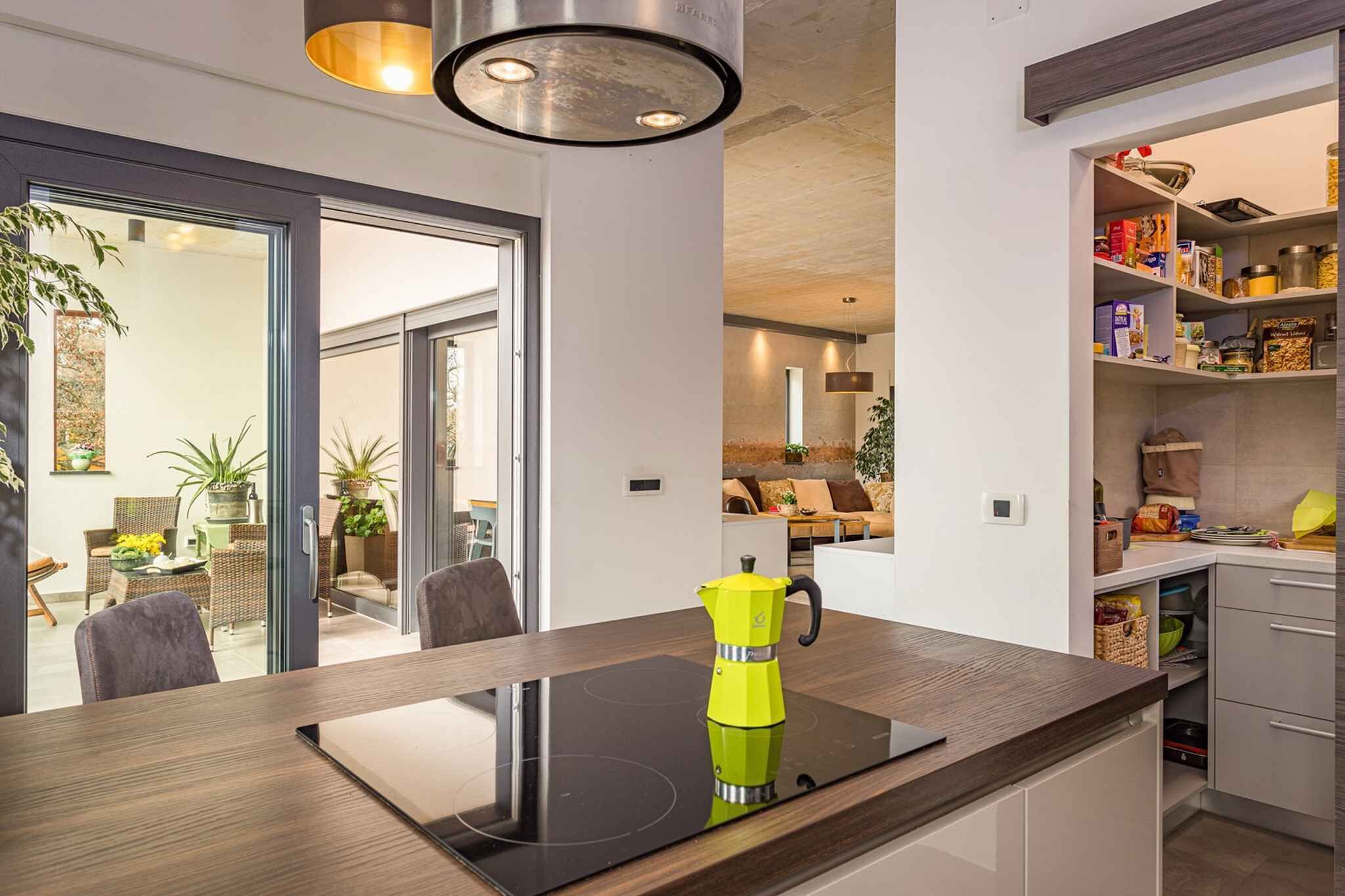 A modern kitchen with a black induction cooktop, a yellow coffee pot, and a built-in pantry with various food items.