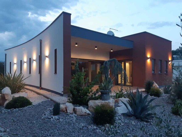 Une maison moderne à la façade incurvée, dotée de nombreuses fenêtres et d’une entrée bien éclairée.