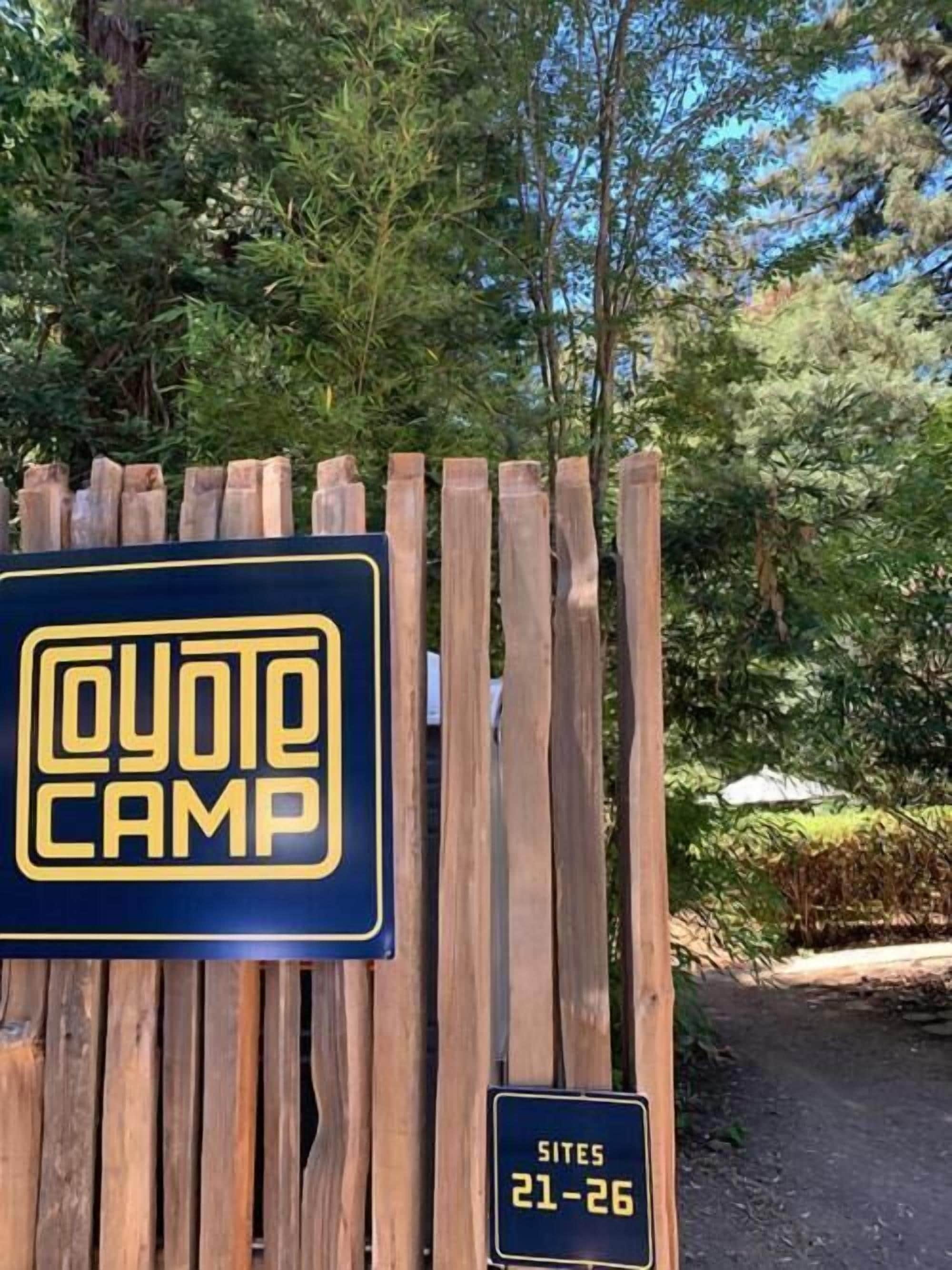 A wooden fence with a sign that reads "Coyote Camp" and another sign indicating "Sites 21-26".