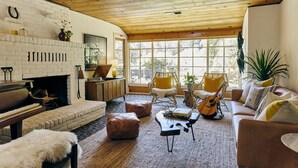 Un salon chaleureux avec une cheminée, un piano, des fauteuils confortables et de grandes fenêtres.