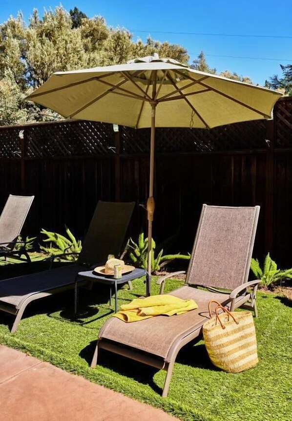 A patio with two lounge chairs, a table, and a large umbrella.