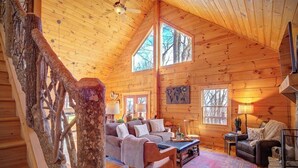 A cozy log cabin interior with a wooden staircase, a sofa set, and a fireplace. - Jacuzzi / Views of Grandfather Mountain / Secluded (Seven Devils)