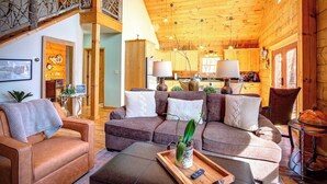 A cozy cabin interior with a wooden ceiling, a living area with sofas and a coffee table, and a kitchen in the background. - Jacuzzi / Views of Grandfather Mountain / Secluded (Seven Devils)
