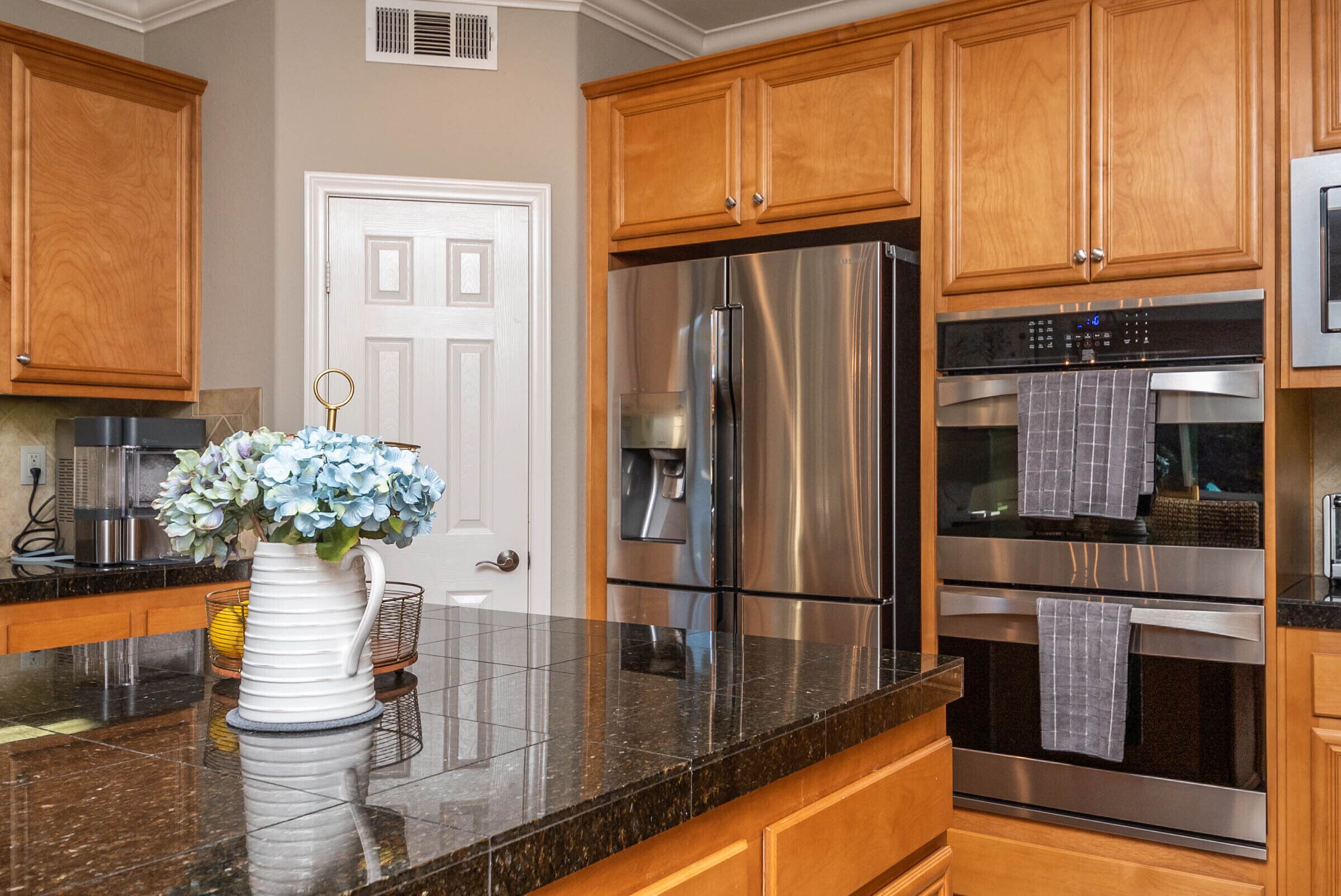 A modern kitchen with wooden cabinets, stainless steel appliances, and a marble countertop.