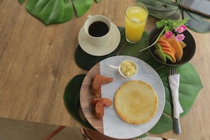 Una escena de desayuno con un plato de comida, una taza de café, un vaso de zumo de naranja y un cuenco pequeño de mantequilla.