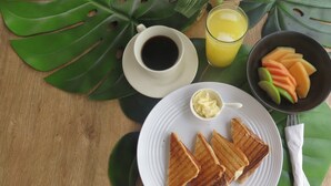 Un plato de desayuno con sándwiches a la plancha, una taza de café, un vaso de zumo de naranja y un bol de fruta.