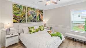 Een slaapkamer met een bed, nachtkastjes, een bankje, een plafondventilator en een raam met jaloezieën.