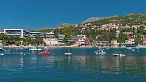 Un pueblo costero con un puerto deportivo lleno de barcos, edificios con tejados rojos y montañas al fondo.
