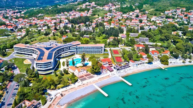 Vista aérea de un pueblo costero con un hotel moderno de diseño curvo, una piscina y una zona de playa.