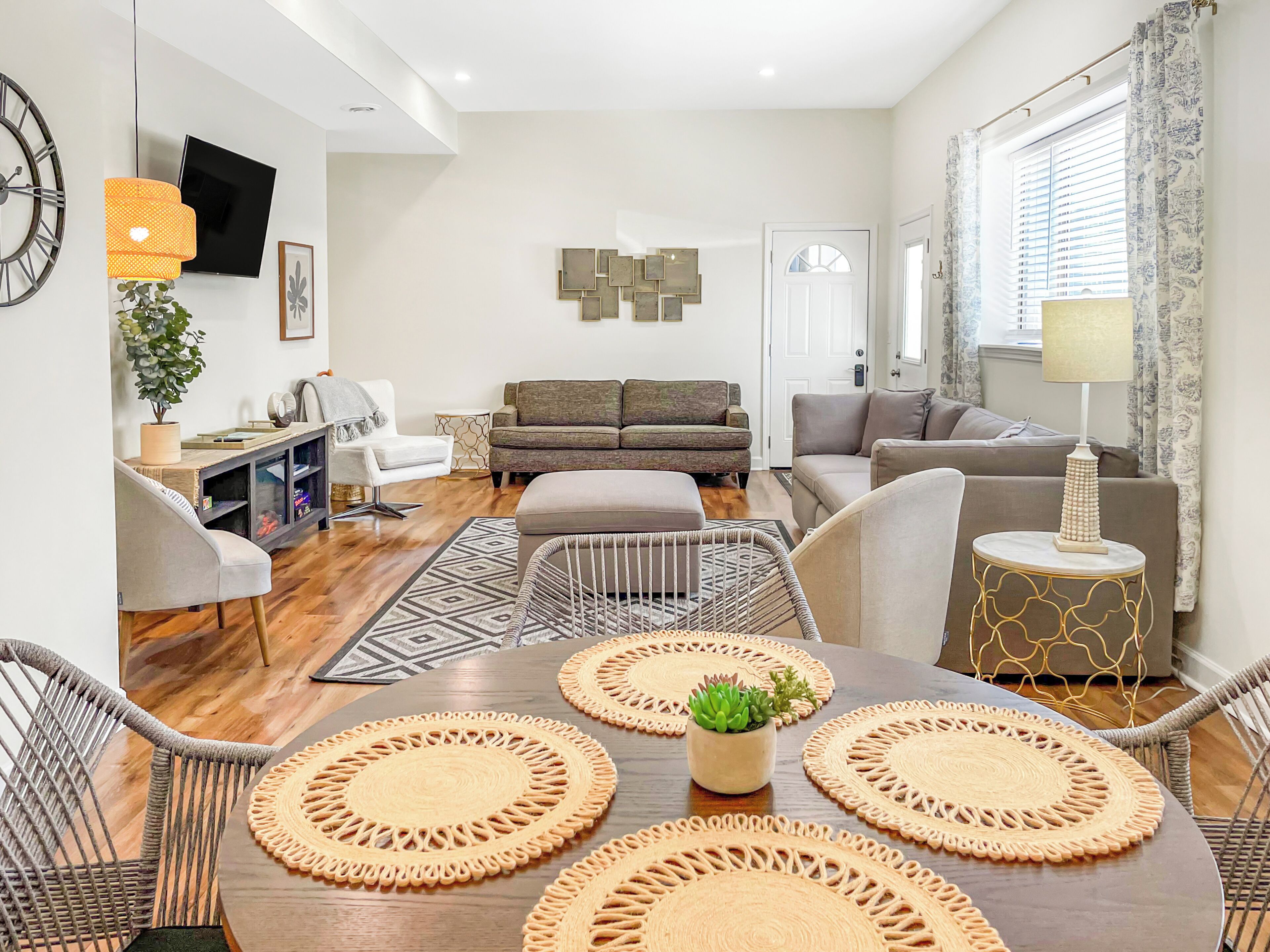 Un salon moderne avec un canapé, des fauteuils, une table à manger avec des sets de table, un téléviseur et une plante.