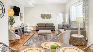 Un salon moderne avec un canapé, des fauteuils, une table à manger avec des sets de table, un téléviseur et une plante.