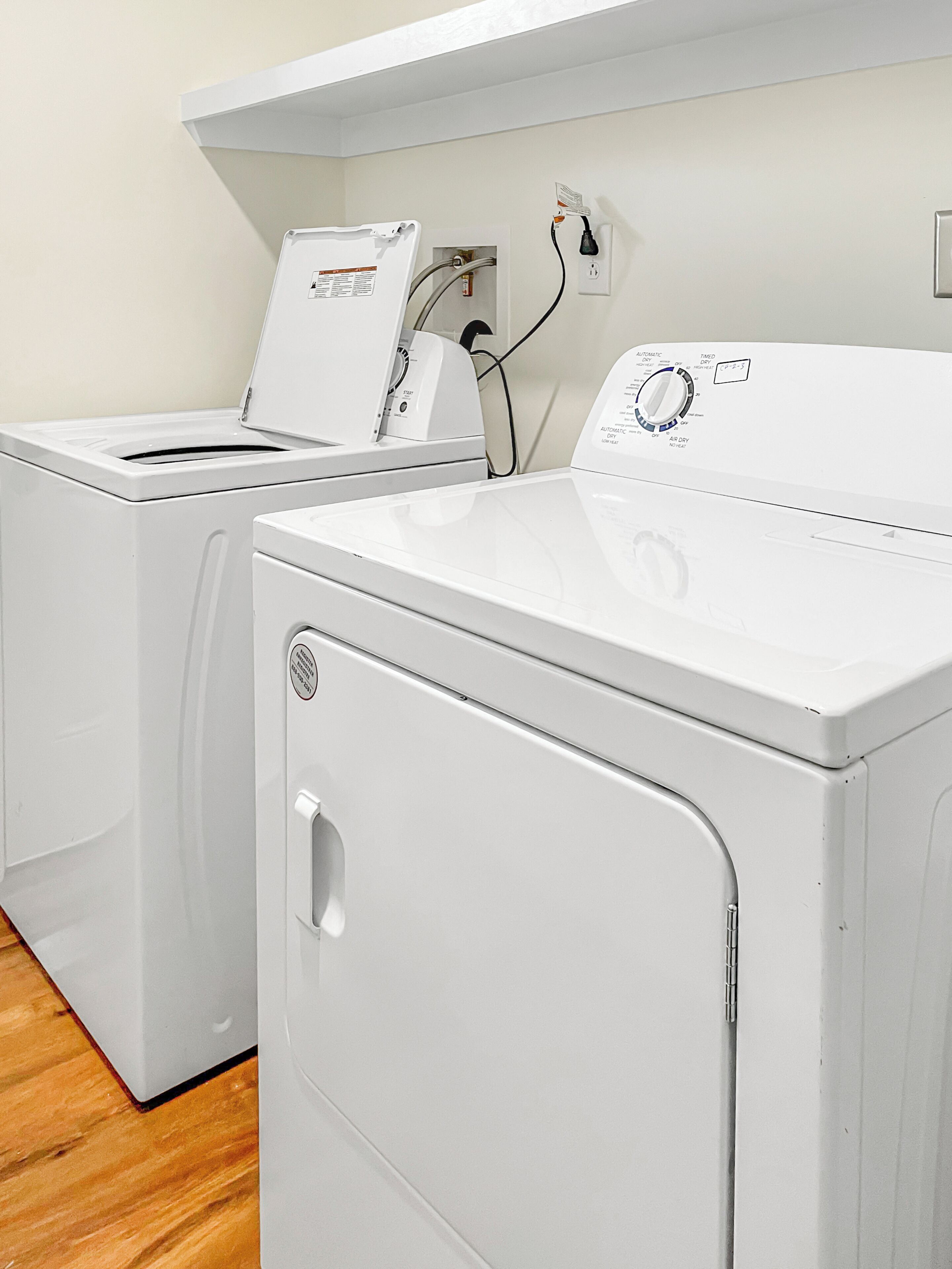 Un espace buanderie comprenant deux machines à laver blanches et un sèche-linge, le tout étant branché à une prise de courant située sur le mur.