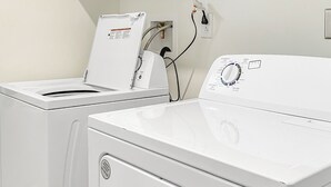 Un espace buanderie comprenant deux machines à laver blanches et un sèche-linge, le tout étant branché à une prise de courant située sur le mur.