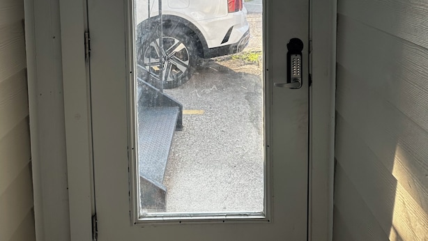 Une porte blanche avec un panneau en verre, un clavier pour ouvrir la porte et une plaque bleue indiquant : « ACCÈS RÉSERVÉ AUX CLIENTS ».
