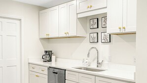 Une cuisine avec des meubles blancs, un lave-vaisselle, un évier et un plancher en bois.