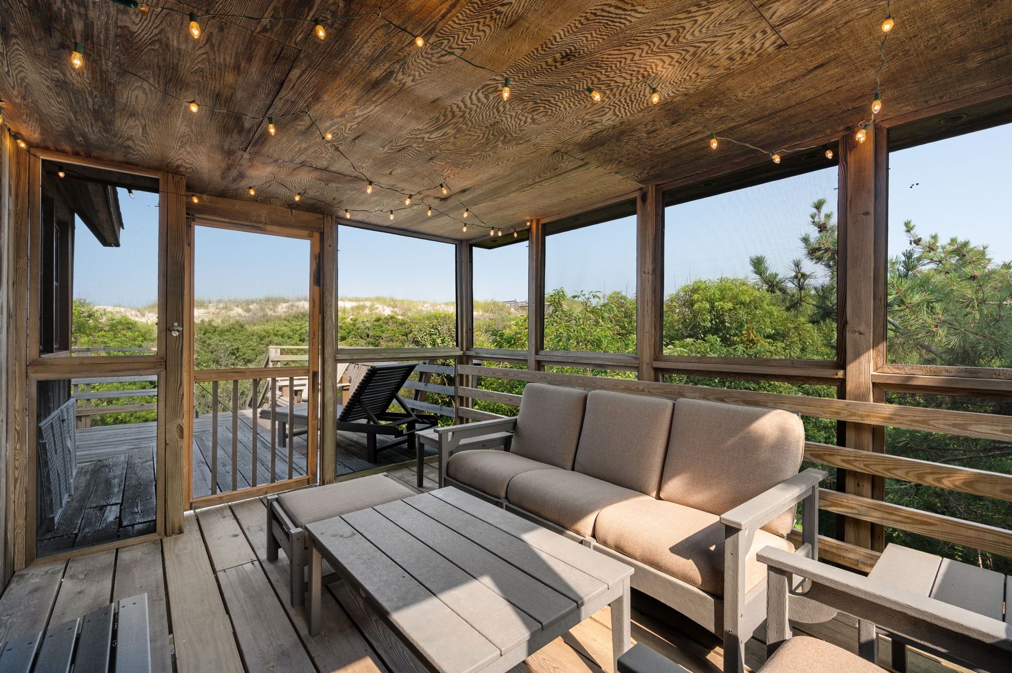 Une terrasse en bois avec un canapé et des fauteuils, donnant sur un paysage naturel.