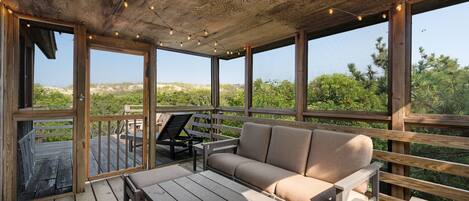 A wooden deck with a sofa and chairs, overlooking a natural landscape.