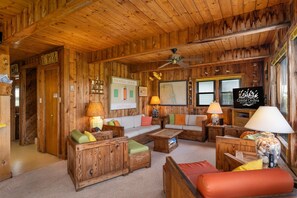 A wooden cabin interior with a sofa set, two lamps, a ceiling fan, and a sign reading "Coastal Carolina Vacation and Sales." - Dunesbury:Oceanfront, dog-friendly, four bedrooms, mini-vacation anytime! (Corolla)