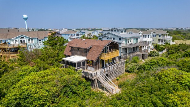 Une maison située sur la côte, dotée d’une terrasse en bois, d’un grand balcon et offrant une vue sur l’océan.