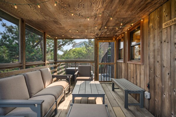 A covered outdoor seating area with a wooden deck, a sofa, a table, and chairs.