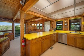 A wooden cabin interior with a kitchen, dining area, and a view of the outdoors.