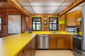 Une cuisine avec des meubles de rangement en bois, un plan de travail jaune, un lave-vaisselle, un évier, une horloge et un four à micro-ondes.
