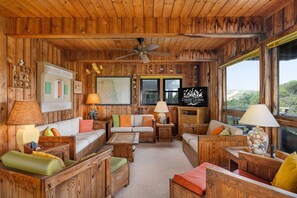 A cozy cabin interior with wooden walls, a ceiling fan, and a sign reading "Coastal Carolina Cottages." - Dunesbury:Oceanfront, dog-friendly, four bedrooms, mini-vacation anytime! (Corolla)