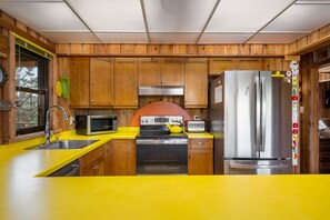 Eine Küche mit Holzschränken, einer gelben Arbeitsplatte, einem Edelstahlkühlschrank, einer Mikrowelle, einem Backofen und einem Spülbecken.