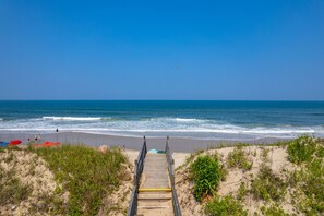 A beach with a wooden walkway leading to the shore, surrounded by sand dunes and vegetation. - Dunesbury:Oceanfront, dog-friendly, four bedrooms, mini-vacation anytime! (Corolla)