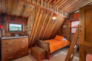 A wooden interior with a bed, dresser, and a window.