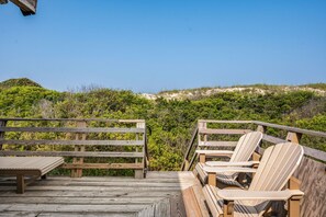 A wooden deck with Adirondack chairs and a table, overlooking a beach with dunes and vegetation. - Dunesbury:Oceanfront, dog-friendly, four bedrooms, mini-vacation anytime! (Corolla)