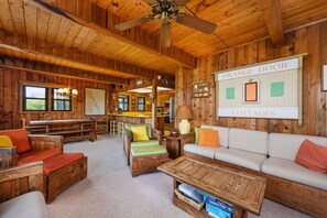 A cozy cabin interior with wooden walls, a ceiling fan, a dining area, and a sign indicating 'Orange Door Cottages.'