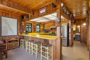 A wooden cabin interior with a kitchen area, bar stools, a refrigerator, and a map on the wall.